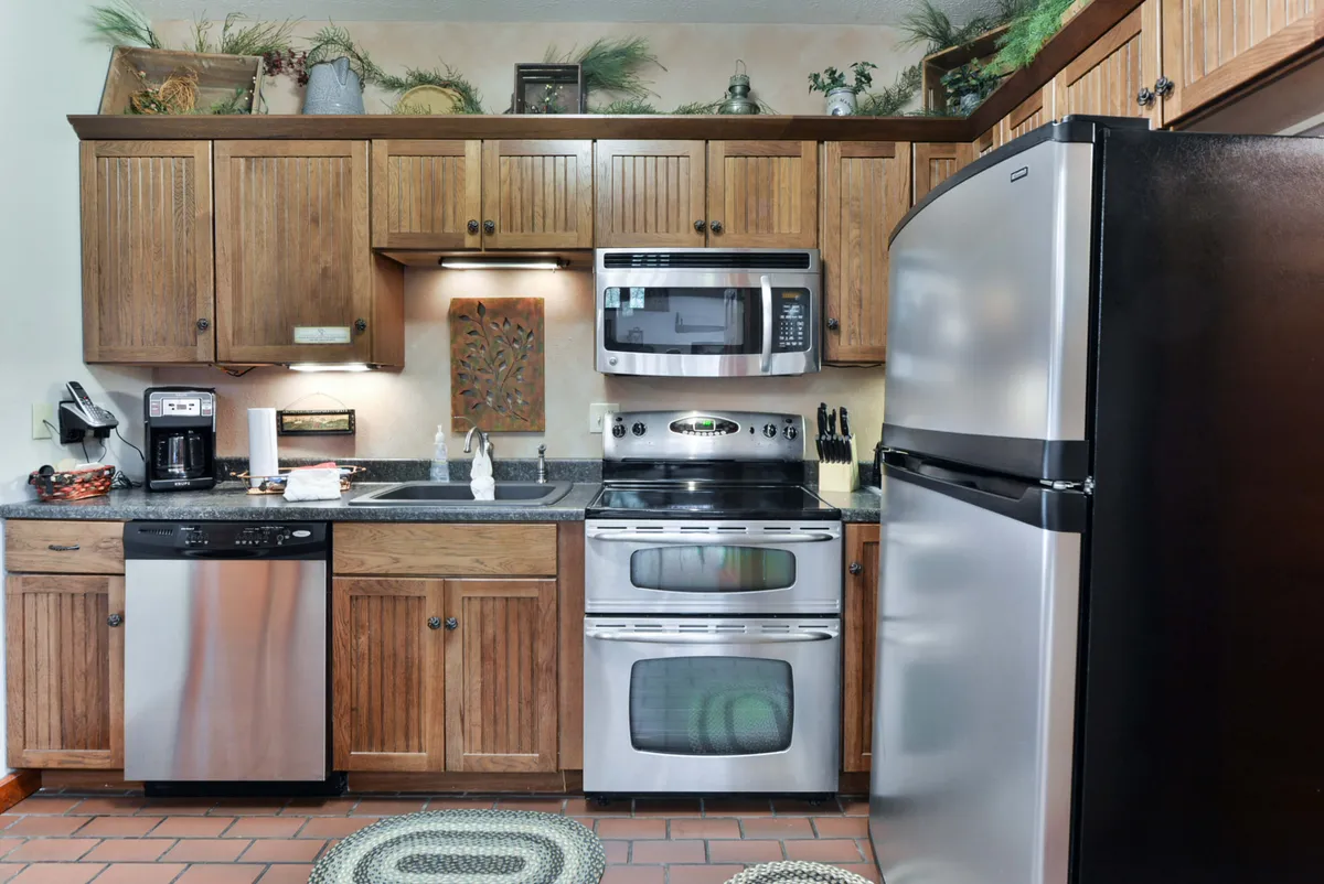 Another angle of a kitchen with stainless steel appliances, wooden cabinets, decorative wall art, and a well-arranged countertop. The scene feels warm and functional, ideal for preparing meals and hosting guests.