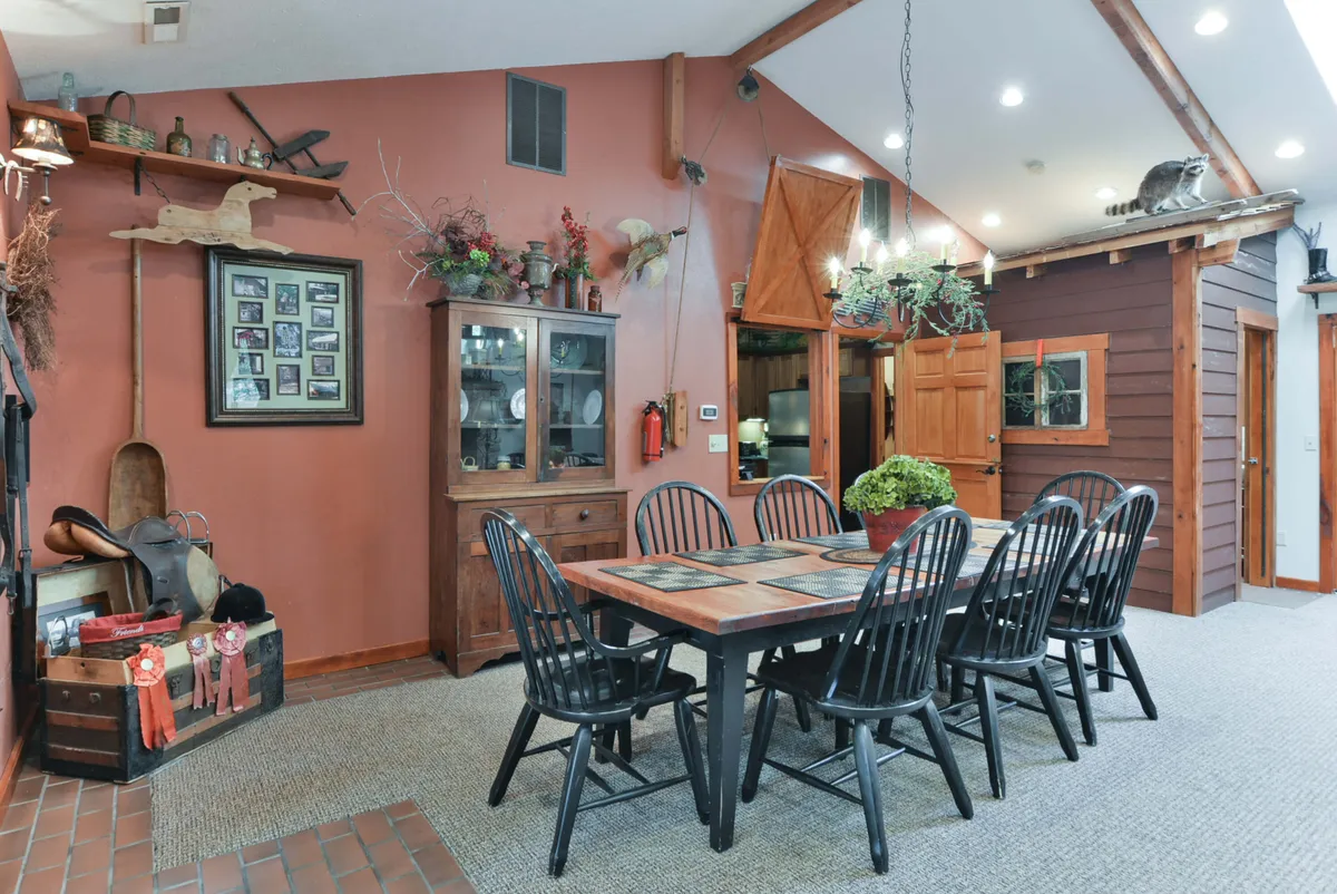 A warm dining space featuring a wooden dining table, a wooden cabinet, decorative wall items including a horse saddle, and a photo collage, all bathed in inviting light. The setup suggests a homely environment for family dinners and gatherings.
