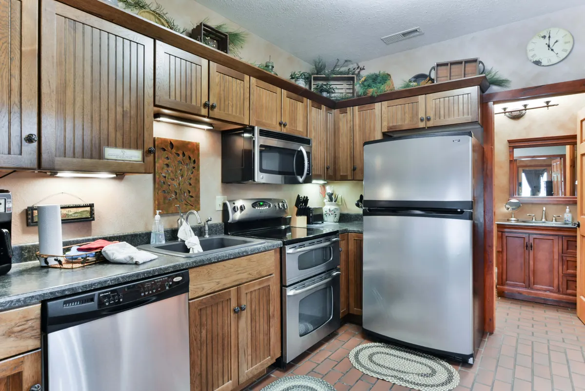 A welcoming kitchen with wooden cabinetry, stainless steel appliances, decorative wall art, a kitchen sink, and a cozy rug. The space is clearly designed for cooking and entertaining, with ample counter space for meal preparation.