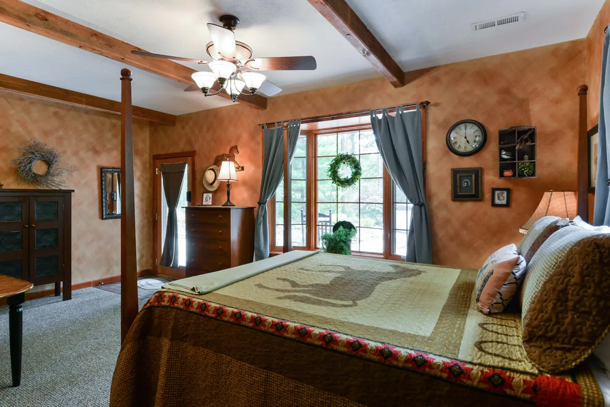 A sunlit bedroom with a four-poster bed, a window letting in natural light, a decorative clock on the wall, and a dresser with a lamp. The setting exudes warmth, comfort, and tranquility, ideal for unwinding after a day’s adventures.