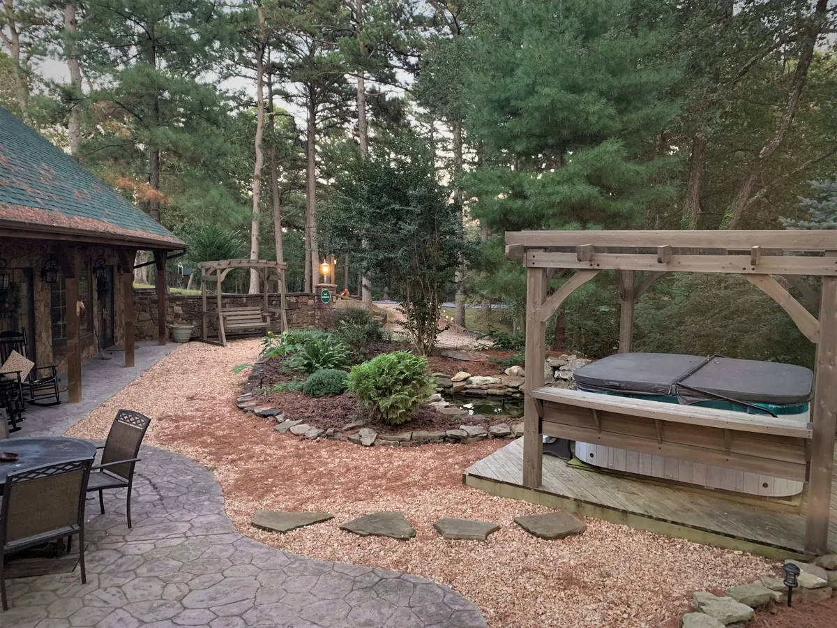 A peaceful garden setting featuring a hot tub, landscaped greenery, a garden pathway, and a cozy sitting area. The ambiance is tranquil and private, ideal for stargazing, soaking, and unwinding after a day of adventure.