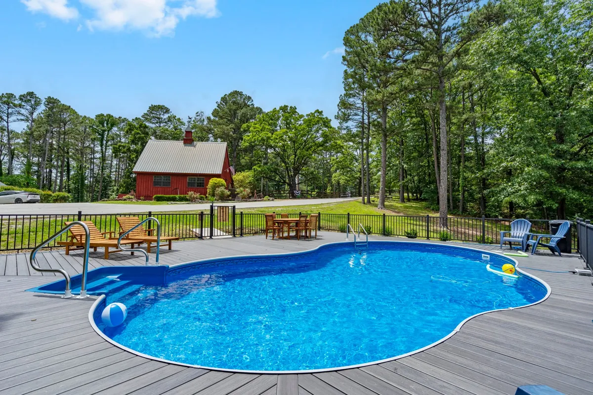 This exterior image showcases a serene saltwater swimming pool adjacent to a red barn, surrounded by lush green trees and inviting deck seating. The tranquil setting is perfect for relaxation, sunbathing, and enjoying the peaceful countryside backdrop.