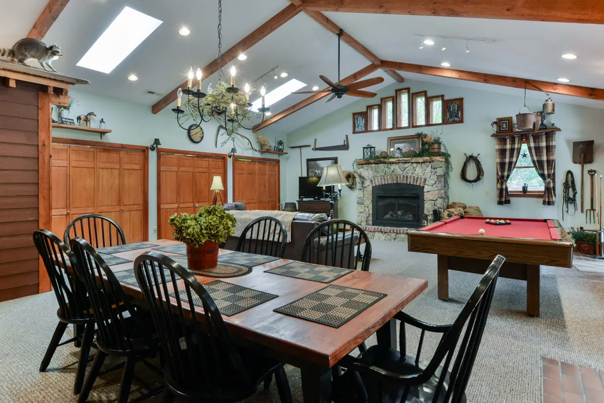 A warm, inviting interior featuring a spacious dining table, a pool table, a fireplace, and wooden cabinetry. The space bridges dining and game areas, reinforcing the open-plan, connected layout described in the section.